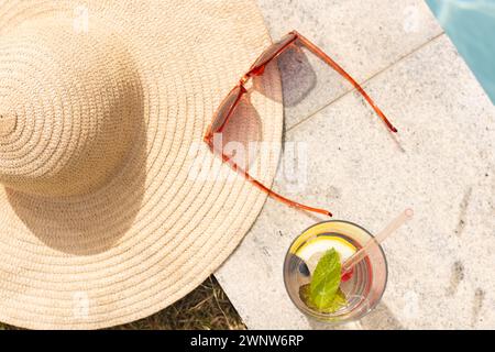 Un cappello di paglia, occhiali da sole e una bevanda rinfrescante siediti sotto la luce del sole con spazio per copiare Foto Stock