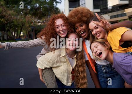 Felici migliori amici multirazziali che si divertono a fare il piggyback per la strada della città. Foto Stock