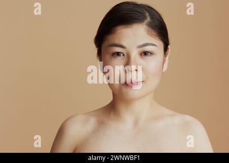 Ritratto di giovane donna asiatica che guarda in macchina fotografica su sfondo beige. Foto Stock