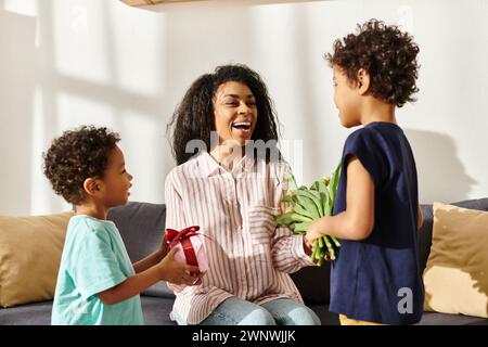 Bella donna afroamericana felice che riceve fiori e regali dai suoi figli piccoli, festa della mamma Foto Stock