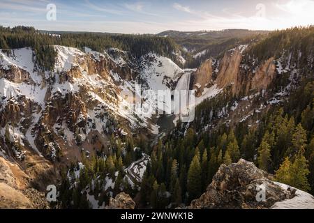 Un'incantevole immagine di una potente cascata che si getta attraverso un paesaggio innevato, tagliando attraverso le aspre scogliere circondate da alberi di pino Foto Stock