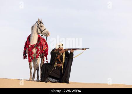 Uomo saudita che caccia nel deserto, puntando il suo fucile Foto Stock