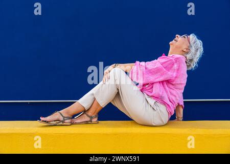 Bella donna anziana felice che indossa abiti casual colorati in posa su sfondo colorato, concetti su anziani e stile di vita Foto Stock