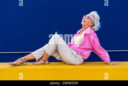 Bella donna anziana felice che indossa abiti casual colorati in posa su sfondo colorato, concetti su anziani e stile di vita Foto Stock