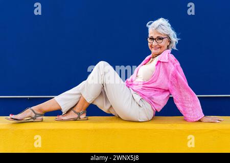 Bella donna anziana felice che indossa abiti casual colorati in posa su sfondo colorato, concetti su anziani e stile di vita Foto Stock