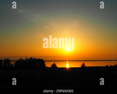 Una bella alba sul lago Onega, Carelia. Il sole in una foschia dorata sorge sopra l'orizzonte e lascia un percorso luminoso solare sulla superficie del Foto Stock