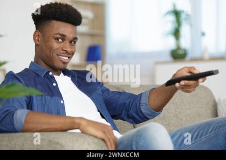 hipster man sul divano che cambia canale tv con telecomando Foto Stock