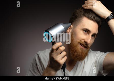 Concetto di cura dei capelli e cura del corpo. L'uomo usa l'asciugacapelli, per fare l'acconciatura dopo aver fatto la doccia e aver asciugato i capelli. Copia spazio Foto Stock