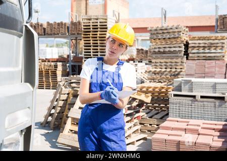 La giovane donna immagazzinatrice fa appunti di lavoro sulla carta nel magazzino Foto Stock