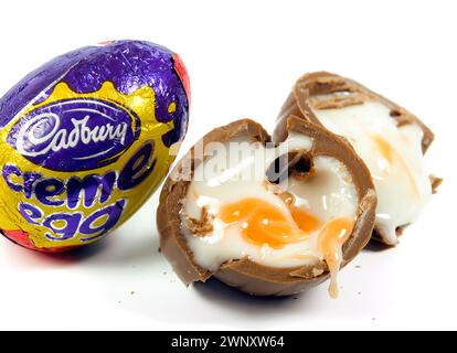 Uova di crema Cadbury su sfondo bianco con una che trasuda un delizioso fondente Foto Stock