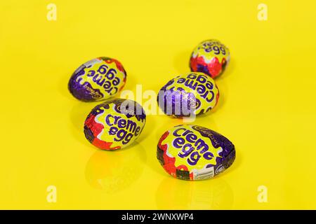 Cinque uova di crema Cadbury su sfondo giallo, uova di Pasqua Foto Stock