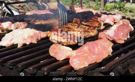 Bistecche di carne di maiale grigliate in carboni bruciati su un barbecue. Crosta croccante. Gustosa bistecca con sangue e strisce fritte. Pezzi pronti fritti e crudi Foto Stock