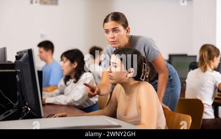 Ritratto di una giovane studentessa che aiuta la sua amica a studiare in classe informatica utilizzando il pc in biblioteca Foto Stock