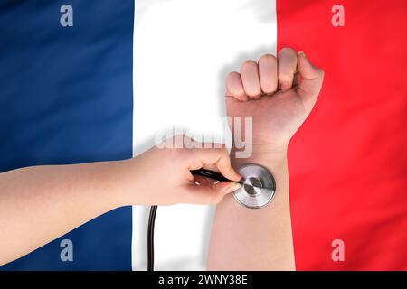 La testa di uno stetoscopio medico sul polso (primo piano) sullo sfondo della bandiera francese. Concetto di sistema sanitario francese Foto Stock