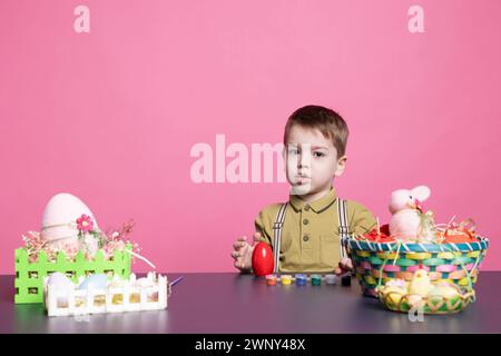 Dolce bambino che si diverte a decorare le uova con francobolli e acquerelli, dipingendo le decorazioni festive per le vacanze della domenica di pasqua. Adorabile bambino adora decorare con attrezzi artigianali. Foto Stock