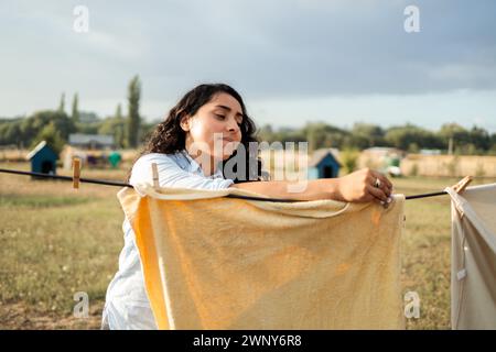 Modest Domestic Scene: La giovane donna latina si occupa di lavanderia asciugando i vestiti nel cortile di campagna. Concetto di lavoro domestico Foto Stock