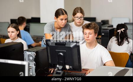 Insegnante che spiega la soluzione del compito a giovani ragazze e ragazzi durante la lezione di informatica Foto Stock