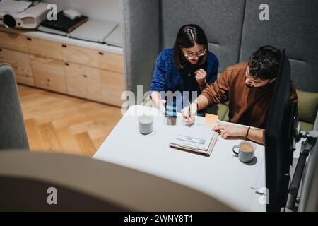 Un uomo e una donna partecipano a una riunione aziendale mirata, analizzando i documenti e utilizzando uno smartphone in uno spazio di lavoro moderno e ben illuminato. Foto Stock