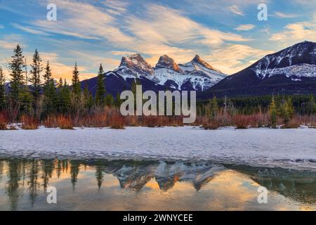 Tramonto invernale d'oro al Three Sisters, un trio di cime vicino a Canmore, Alberta, Canada, nelle Montagne Rocciose canadesi, con alpenglow sulle montagne rif Foto Stock