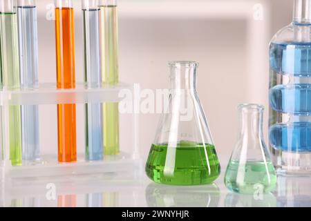 Analisi di laboratorio. Vetreria diversa con liquidi su tavolo bianco su sfondo sfocato Foto Stock