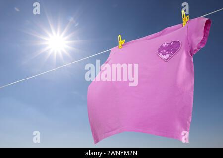 T-shirt viola che si asciuga sulla linea di lavaggio contro il cielo blu, vista ad angolo basso Foto Stock