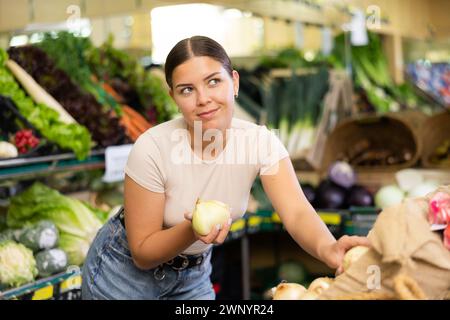 Giovane donna acquirente sceglie cipolle nel supermercato Foto Stock