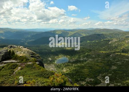 Vista dalla cima della montagna fino alla densa taiga sui crinali e a un piccolo e pittoresco lago in pianura. Parco naturale Ergaki, Krasnoyarsk regio Foto Stock