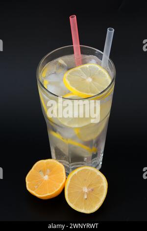 Rinfrescante limonata in un alto vetro sfaccettato con ghiaccio e fette di limone su sfondo nero. Primo piano. Foto Stock