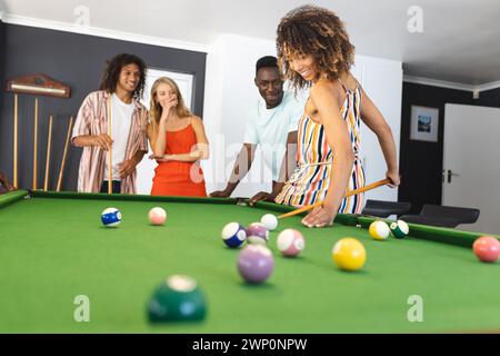 Un gruppo eterogeneo di amici ama giocare a biliardo, concentrandosi su una donna birazziale che le spara Foto Stock