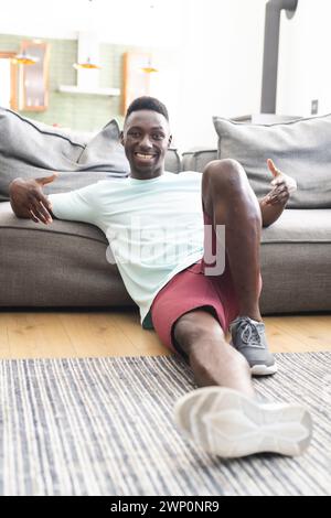 Il giovane afroamericano in un abbigliamento casual siede sul pavimento, sorridendo alla macchina fotografica Foto Stock