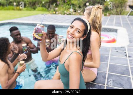 Una giovane donna birazziale in costume da bagno verde si gode una festa in piscina con gli amici Foto Stock