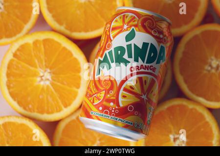 KIEV, UCRAINA - 7 LUGLIO 2023 bevanda all'arancia Mirinda con molte arance fresche su sfondo colorato Foto Stock