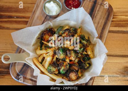 Un piatto di patatine fritte e cavolini di bruxelles è servito su un vassoio di legno Le patatine fritte sono dorate e i germogli sono verdi e croccanti. Il piatto loo Foto Stock