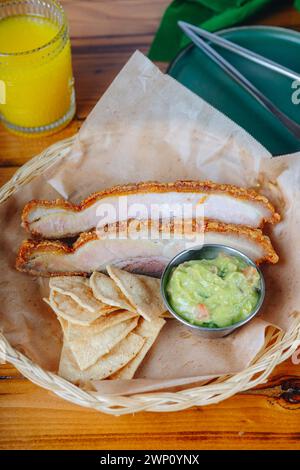 Un piatto di carne e patatine con un lato di guacamole. Il piatto si trova su un tavolo di legno e sullo sfondo c'è un bicchiere di succo d'arancia Foto Stock