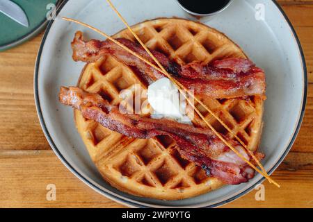 Un piatto di pancetta e waffle con uno stick al centro. La pancetta è cotta e i waffle sono dorati. Il piatto è su un tavolo di legno Foto Stock