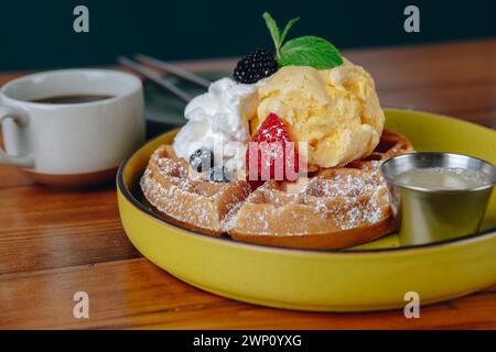 Un piatto di waffle con panna montata e fragole sopra si trova su un tavolo accanto a una tazza di caffè Foto Stock