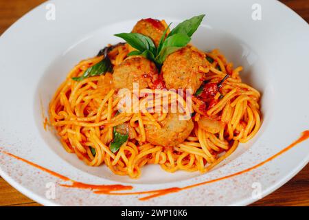 Un piatto di spaghetti con polpette e basilico. Il piatto è servito su un piatto bianco e ha una salsa rossa sgocciolata sulla parte superiore Foto Stock