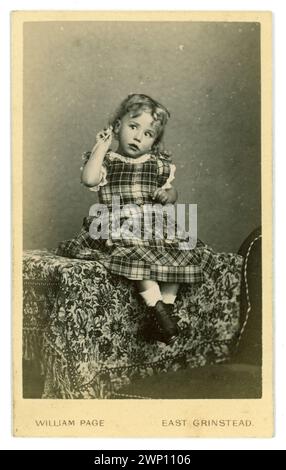 Originale, affascinante carte de visite vittoriana (biglietto da visita o CDV) di dolce bambino vittoriano con capelli ricci, stivali con bottoni, un bellissimo vestito tartan, che regge un ciondolo magari con un sonaglino mentre sembra che stia ascoltando un suono, i ragazzi indossavano anche abiti simili in questo periodo. Dallo studio di William Page, Moat House, East Grinstead, West Sussex, Regno Unito circa 1864 Foto Stock