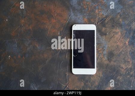 Telefono bianco con schermo rotto su sfondo scuro Foto Stock