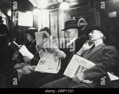 Vista che guarda due passeggeri maschi e due femmine nel vano treno. L'uomo in primo piano dorme velocemente mentre l'uomo alla sua destra regge la sua copia di "The Times". Londra. 1937 Foto Stock