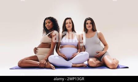 Le donne in attesa si dedicano allo yoga, nutrendo i loro piccoli urti in una diversa classe di fitness. Le mamme che saranno in grado di dare la priorità alle cure prenatali nel loro terzo trimestre Foto Stock