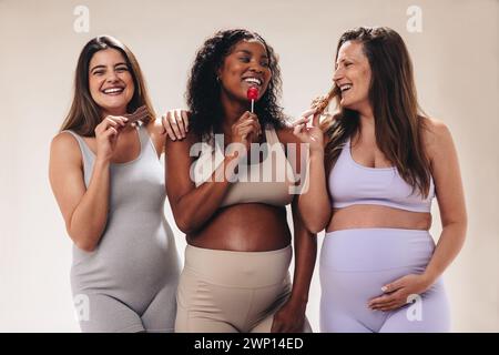 Un gruppo eterogeneo di donne incinte che si riuniscono in uno studio e che desiderano dolci come caramelle e cioccolato. Aspettandosi che le madri si godano un Foto Stock