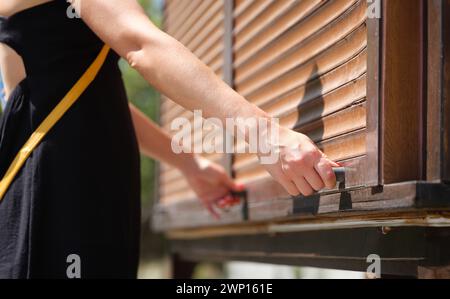 Le mani femminili tengono le maniglie del fermo di legno aprono le tende di legno all'aperto closeup Foto Stock