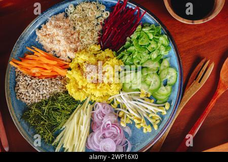 Un piatto blu con una varietà di verdure, tra cui carote, cetrioli e sedano. La piastra è posizionata su un tavolo di legno con una forchetta e un cucchiaio nelle vicinanze Foto Stock