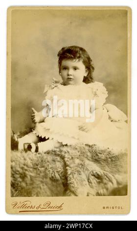 Originale e affascinante carte de visite vittoriane (biglietto da visita o CDV) di giovane ragazza vittoriana, bambino vittoriano, di circa 2 anni, con capelli ricci scuri, tappeto di pelliccia seduto, Villiers & Quick, 42 Park Street, Bristol, Regno Unito verso la fine degli anni '1880 Foto Stock