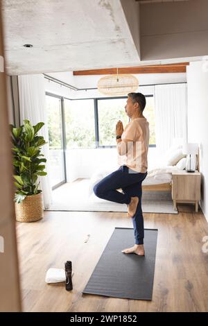 L'anziano birazziale pratica yoga in una sala luminosa e moderna Foto Stock