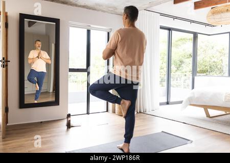 L'anziano birazziale pratica yoga in una camera luminosa e moderna Foto Stock