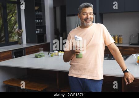 Senior man birazziale che regala un frullato verde in una cucina moderna Foto Stock