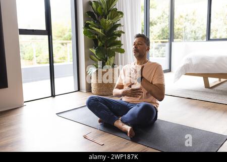 L'anziano birazziale pratica yoga in una tranquilla camera da letto Foto Stock