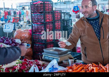 Un uomo che paga per fare shopping in un mercato locale. Foto Stock